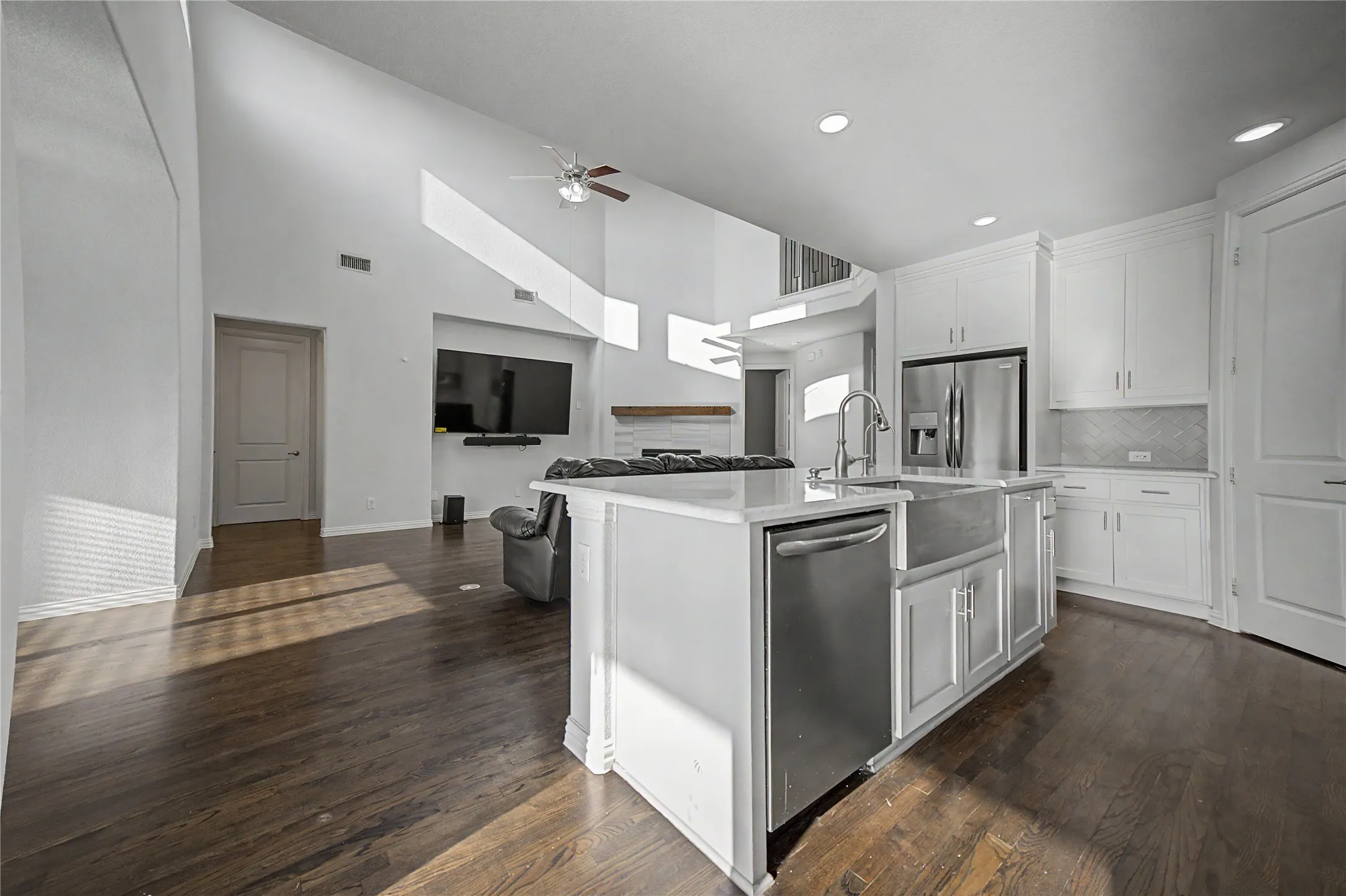 Vaulted ceilings, wood-finish flooring, white cabinetry, stainless steel appliances, and an island with a farmhouse sink