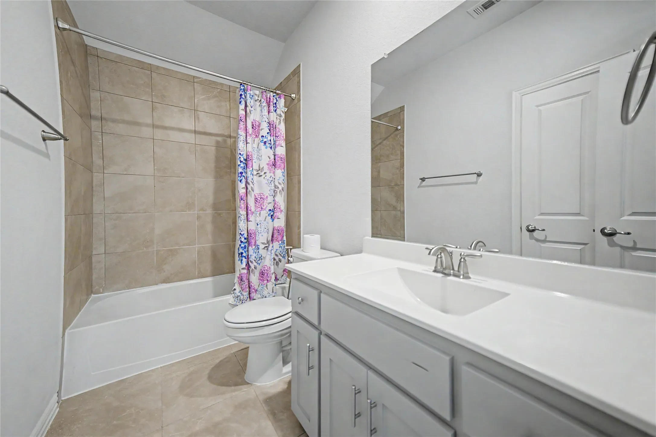 Tiled shower surround with a white tub, single vanity with a white countertop, and an expansive wall mirror