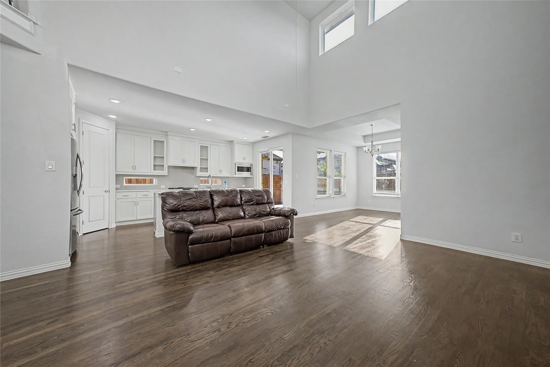 Vaulted ceilings with high windows, dark wood-finish flooring, white cabinetry, recessed lighting, and stainless steel appliances