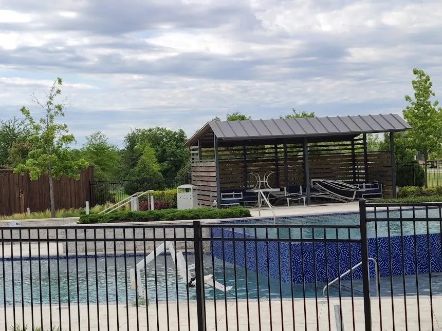 Swimming pool featuring a blue mosaic tile wall, a surrounding concrete deck, and a black metal fence