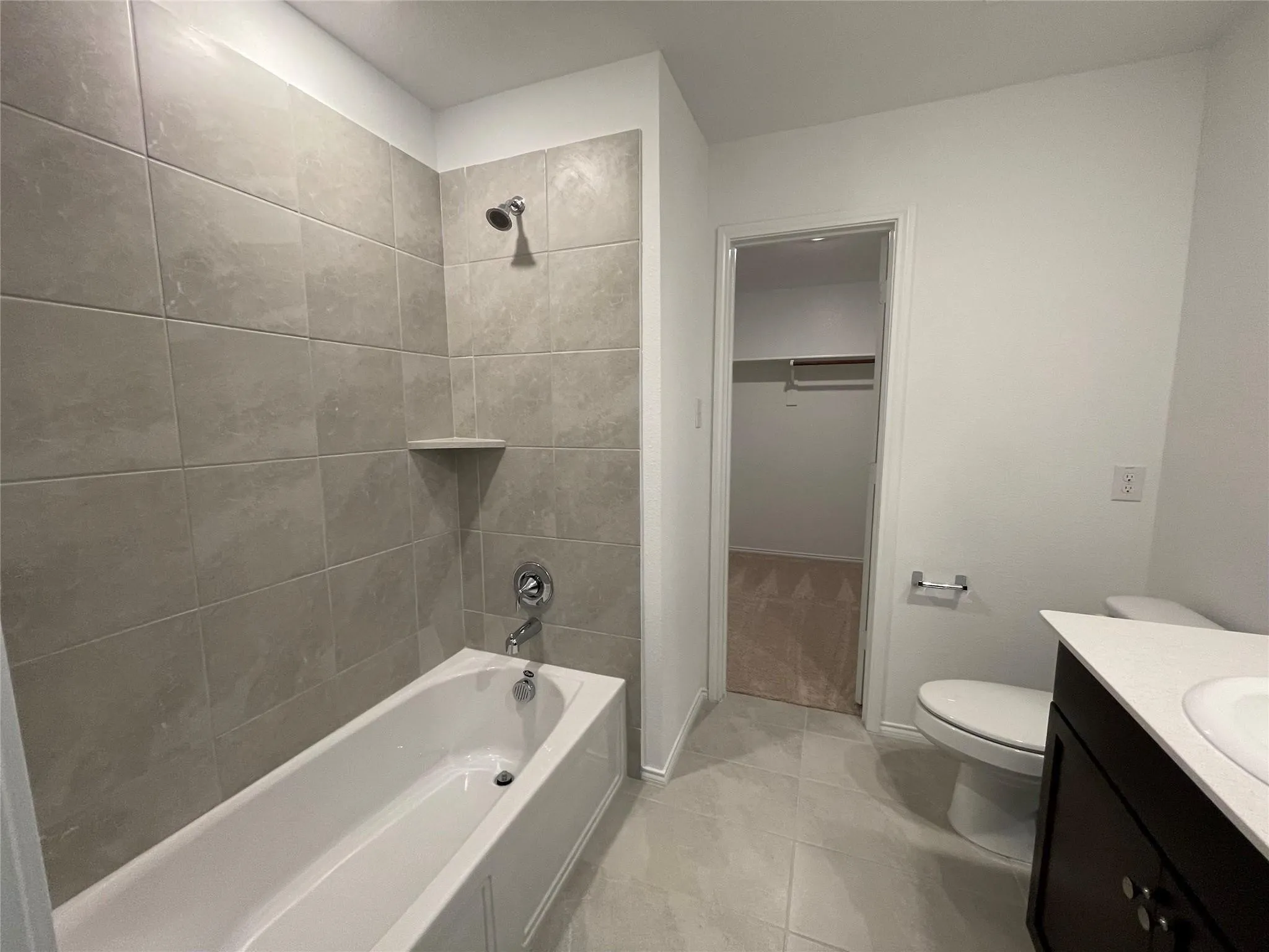 Bathroom featuring a bathtub with tiled surround, chrome fixtures, dark wood-finish vanity with countertop, and toilet