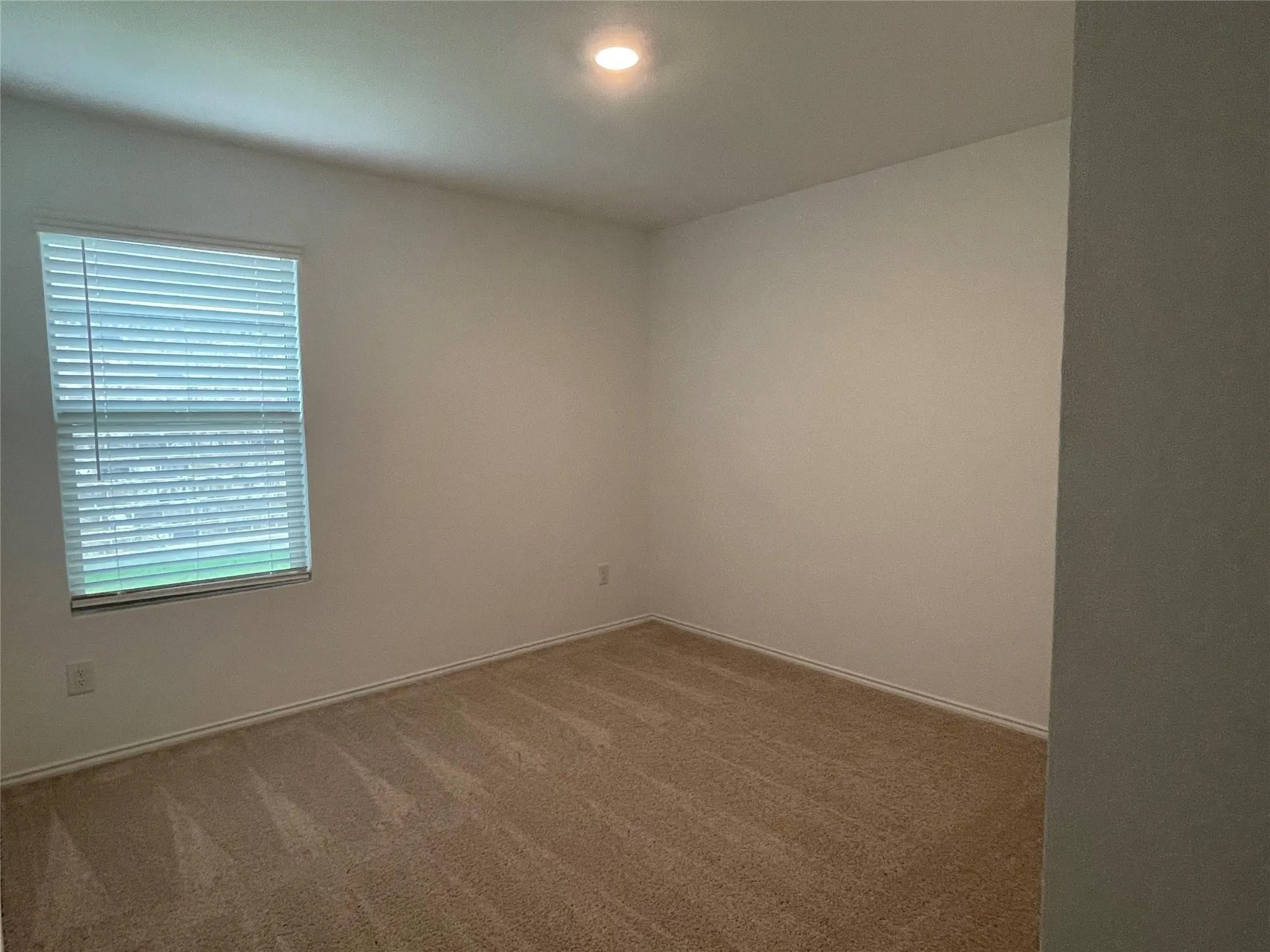 Recessed lighting and a window with blinds illuminate this carpeted room