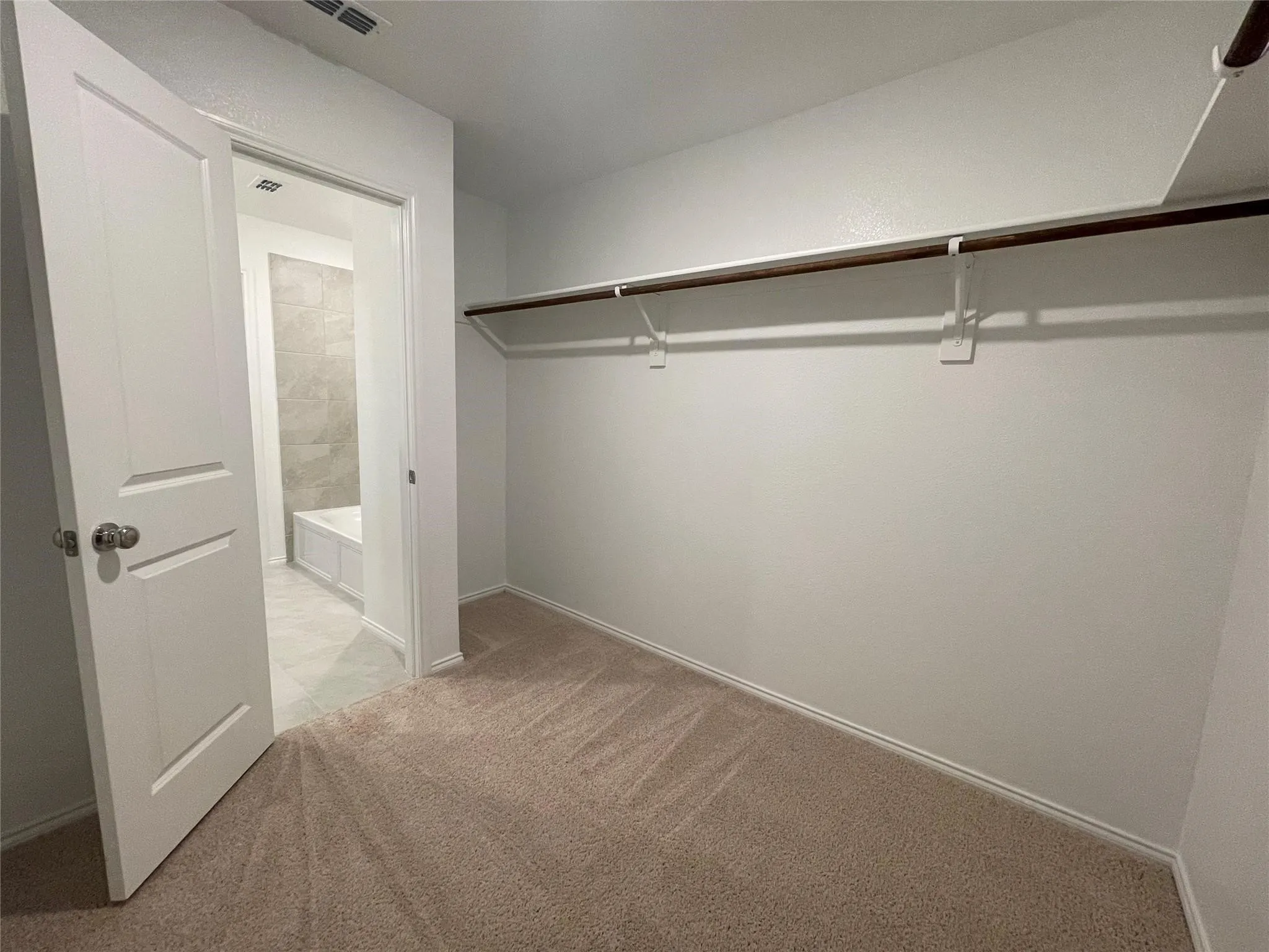 Neutral-toned carpeted flooring, white walls, and a built-in closet rod