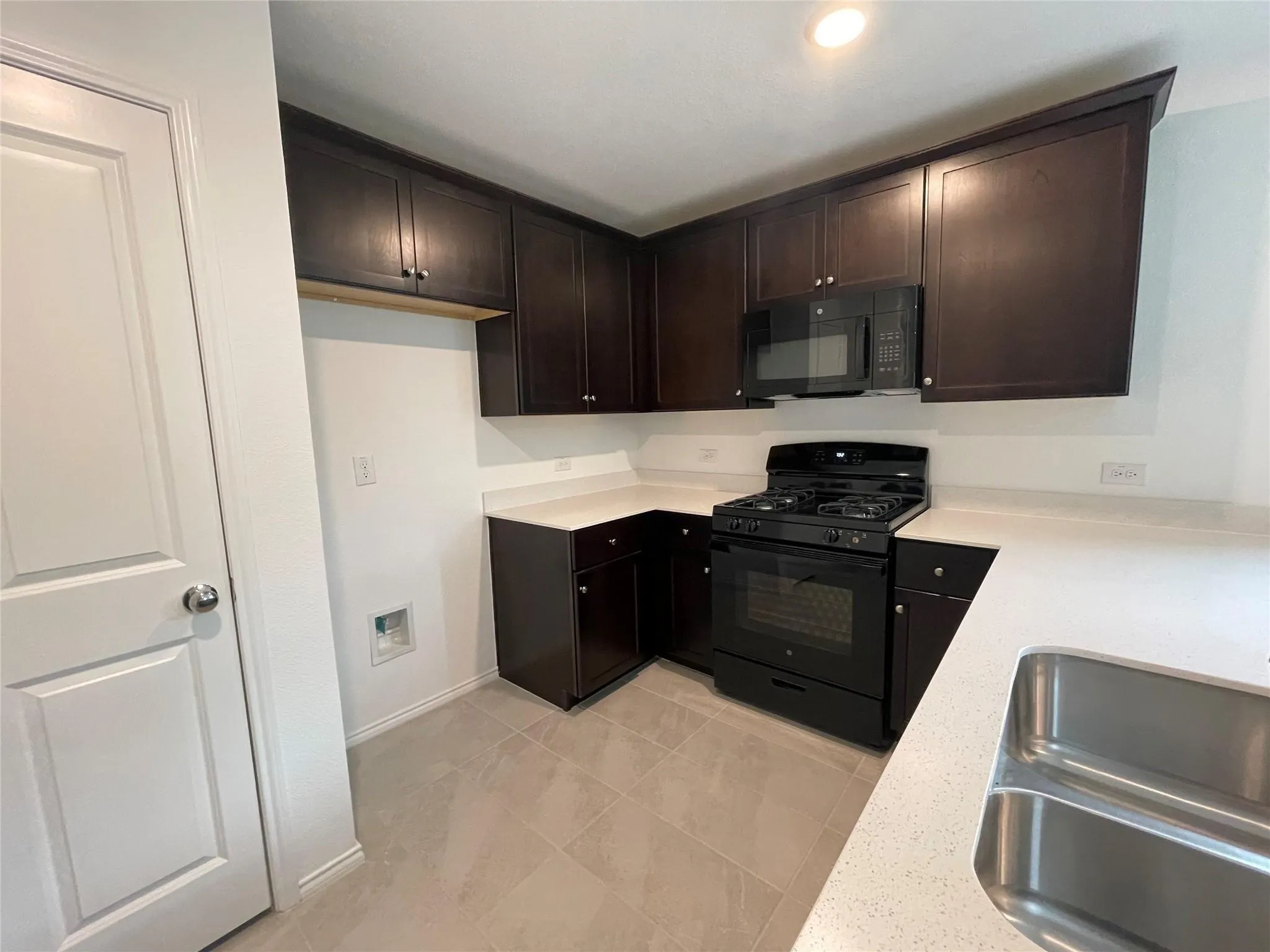 Kitchen featuring dark wood-finish cabinetry, light-toned countertops, tile flooring, a built-in microwave, and a gas range