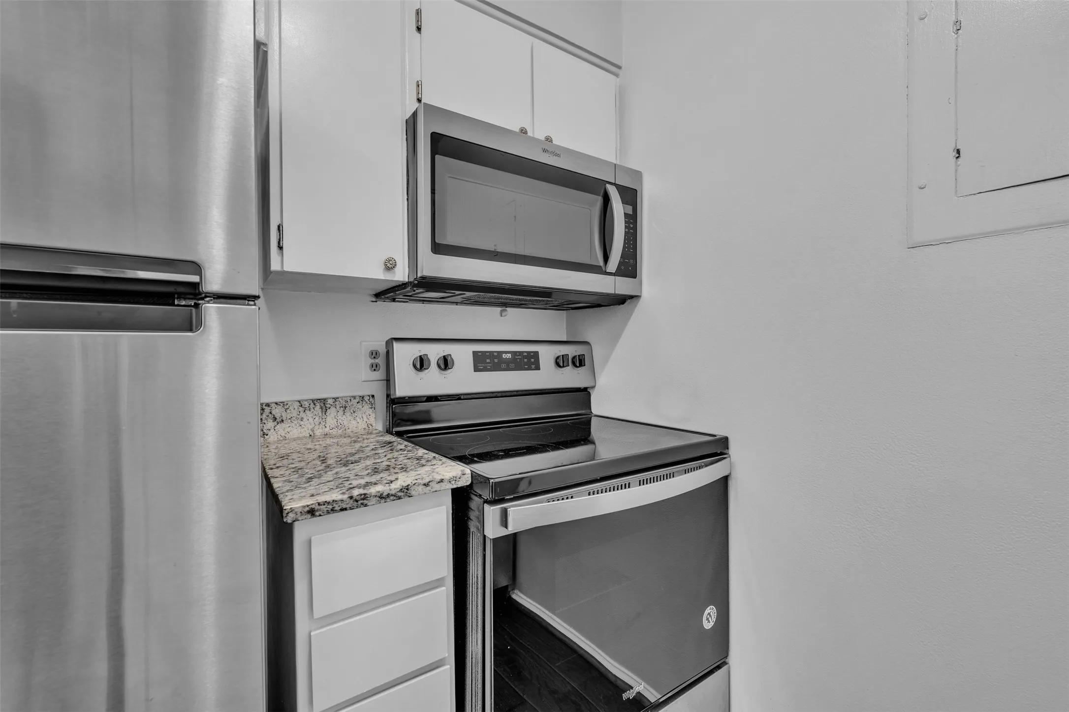 Stainless steel refrigerator, stainless steel microwave, stainless steel range, white cabinetry, and granite-style countertop