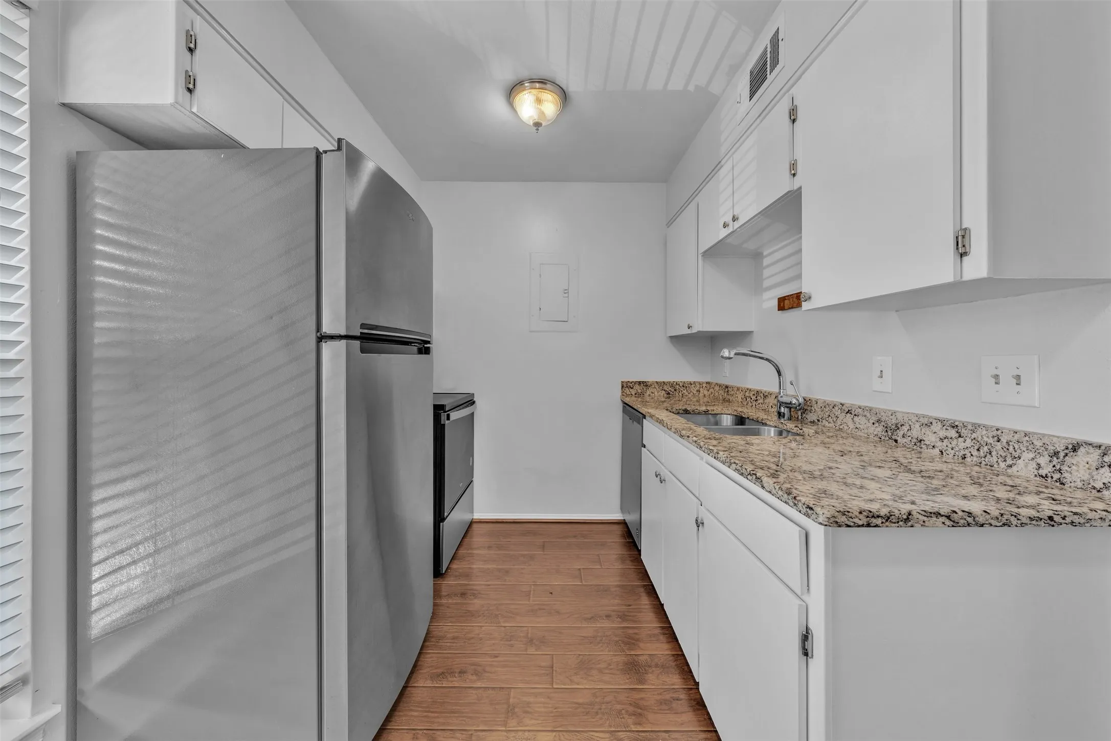 Stainless steel refrigerator, white cabinetry, granite-style countertop, stainless steel sink, wood-finish flooring