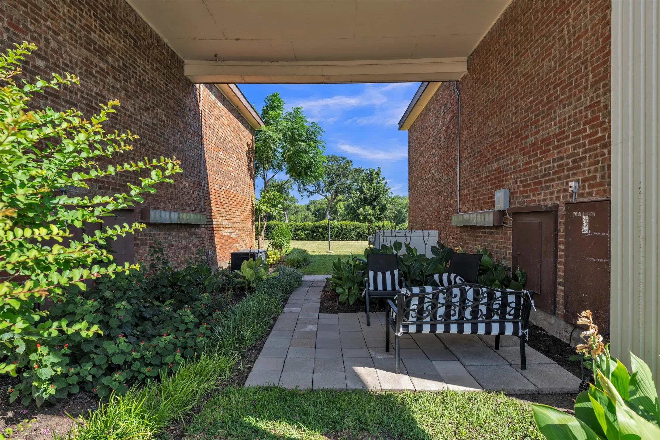 Covered outdoor patio with a paver stone surface, brick exterior walls, and surrounding landscaping