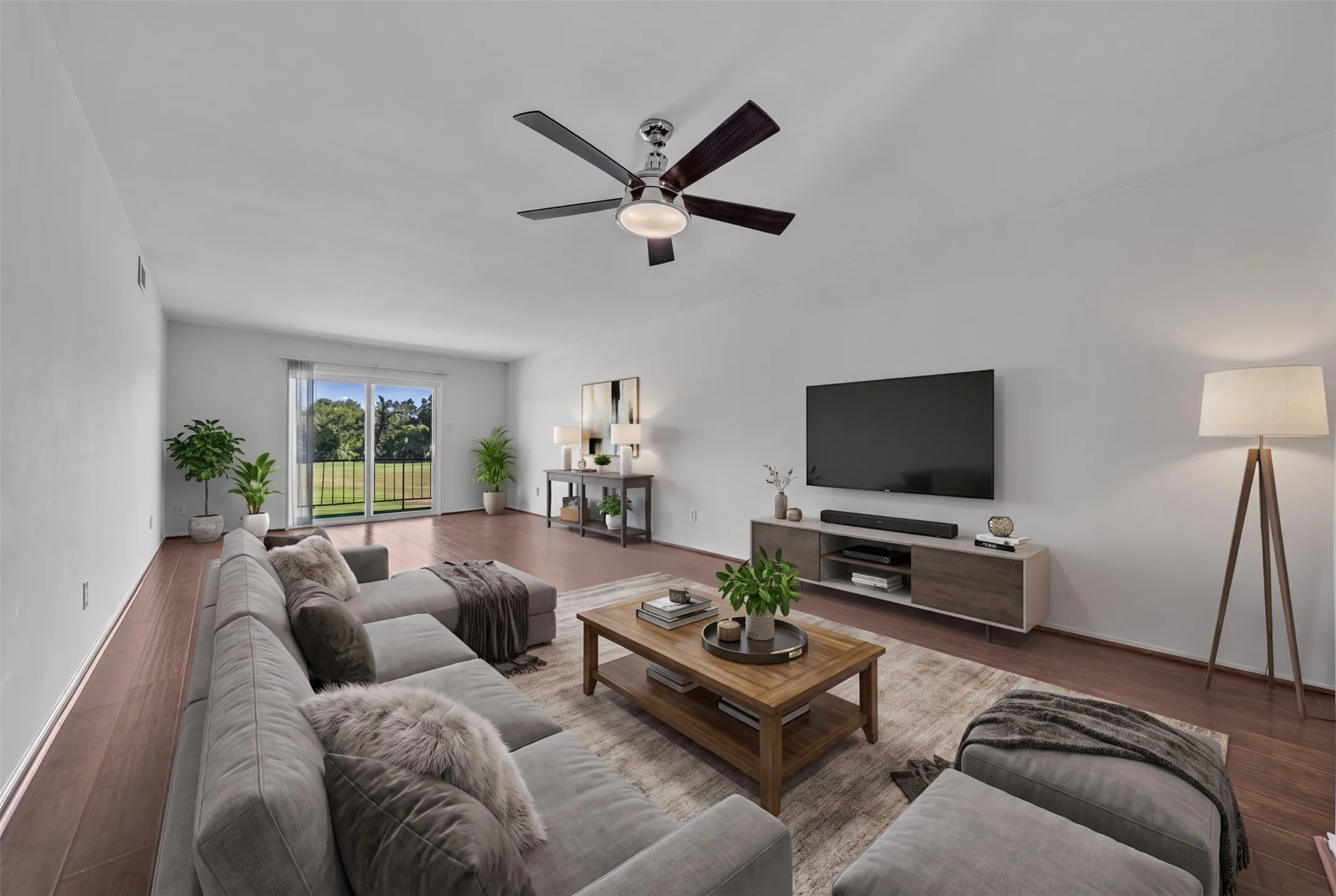 Spacious living area featuring wood-finish flooring, a ceiling fan with integrated lighting, and a sliding glass door leading to a balcony
