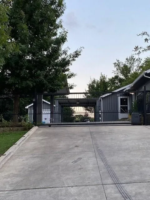 Concrete driveway with a black metal gate, flanked by a shiplap-sided building