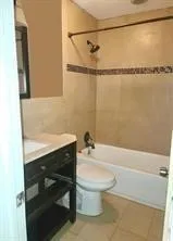 Tile flooring, built-in bathtub, tile shower surround with decorative accent, dark wood-finish vanity, and integrated sink