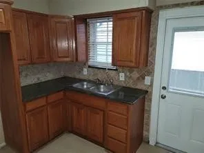 Wood-finish cabinetry paired with dark countertops, a tiled backsplash, and a double basin sink