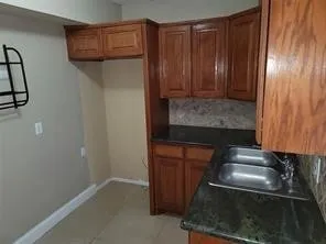 Wood-finish cabinetry with a double basin stainless steel sink, dark countertop, and tiled backsplash