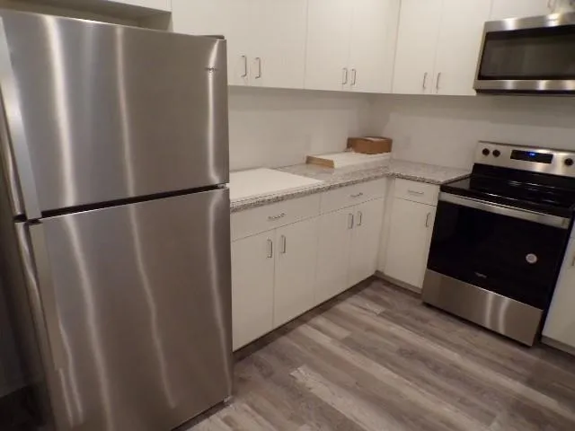 Stainless steel appliance suite, white cabinetry with silver-tone hardware, light-toned countertops, and wood-finish flooring
