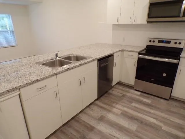 Kitchen featuring light-toned countertops, white cabinetry, a stainless steel double basin sink, and wood-finish flooring