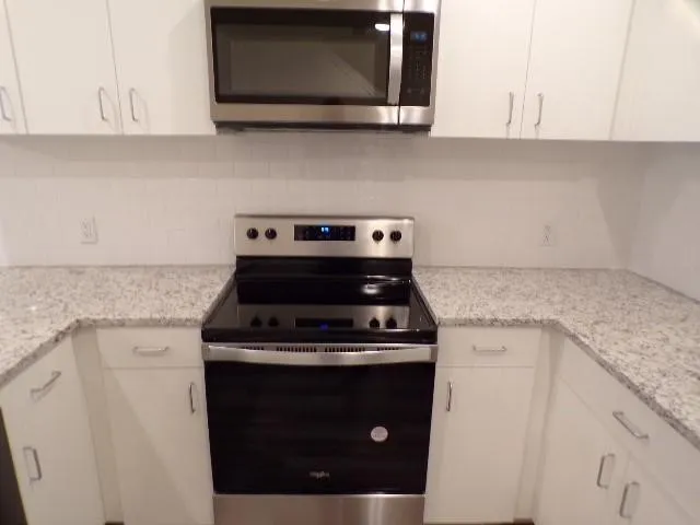 U-shaped kitchen with white cabinetry, stainless steel appliances, speckled countertops, white subway tile backsplash, and an over-the-range microwave