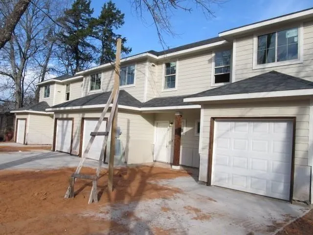 Multi-unit property with light-colored siding, multiple individual garages, and dark-shingled roofs