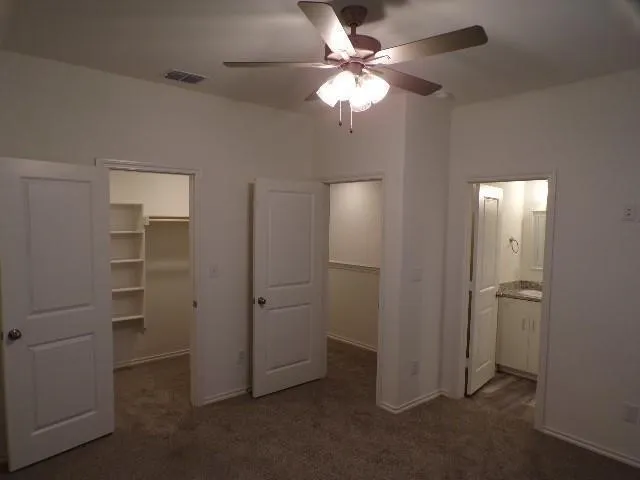 Carpeted room featuring a ceiling fan with integrated lighting, two panel doors, and two walk-in closets with built-in shelving