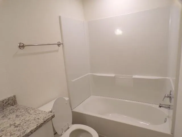 White acrylic bathtub with integrated shower, chrome-finish fixtures, and a light-toned granite countertop