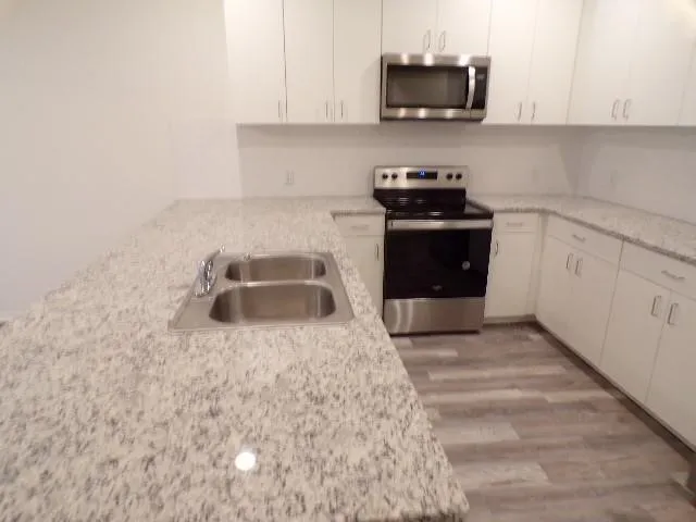 U-shaped kitchen featuring white cabinetry, light-toned countertops, a double basin stainless steel sink, a stainless steel microwave, and a stainless steel range