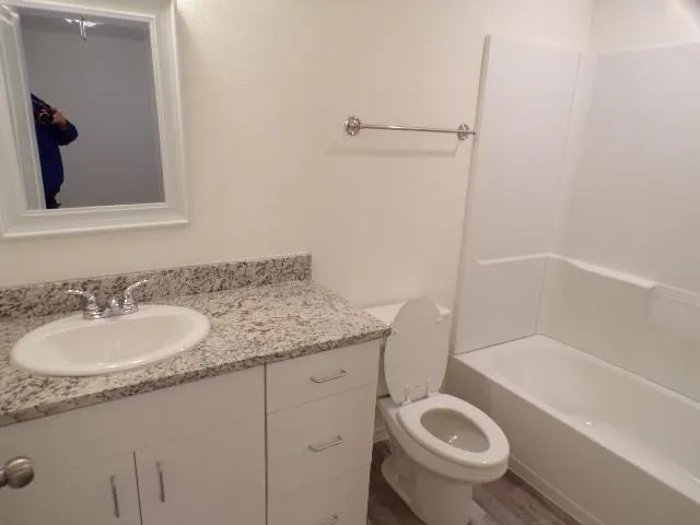 White vanity cabinet with integrated drawers and doors, gray flecked countertop, polished chrome faucet, white framed mirror, and a white bathtub with a shower surround