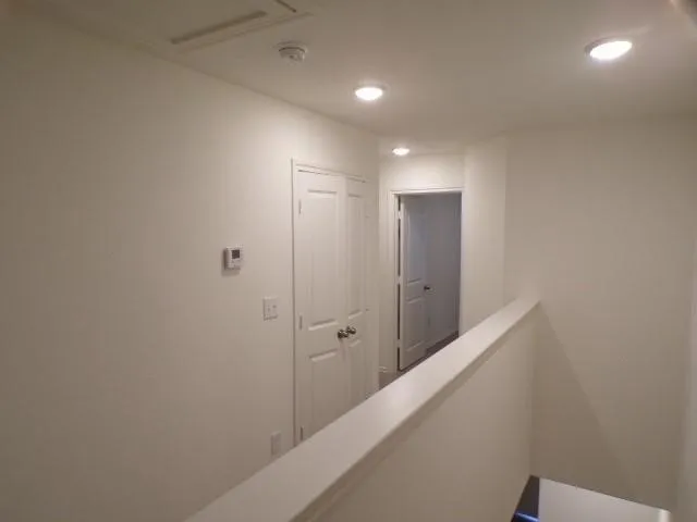 Recessed lighting illuminates the upper hallway with a clean white palette, featuring interior doors with lever handles and a thermostat control