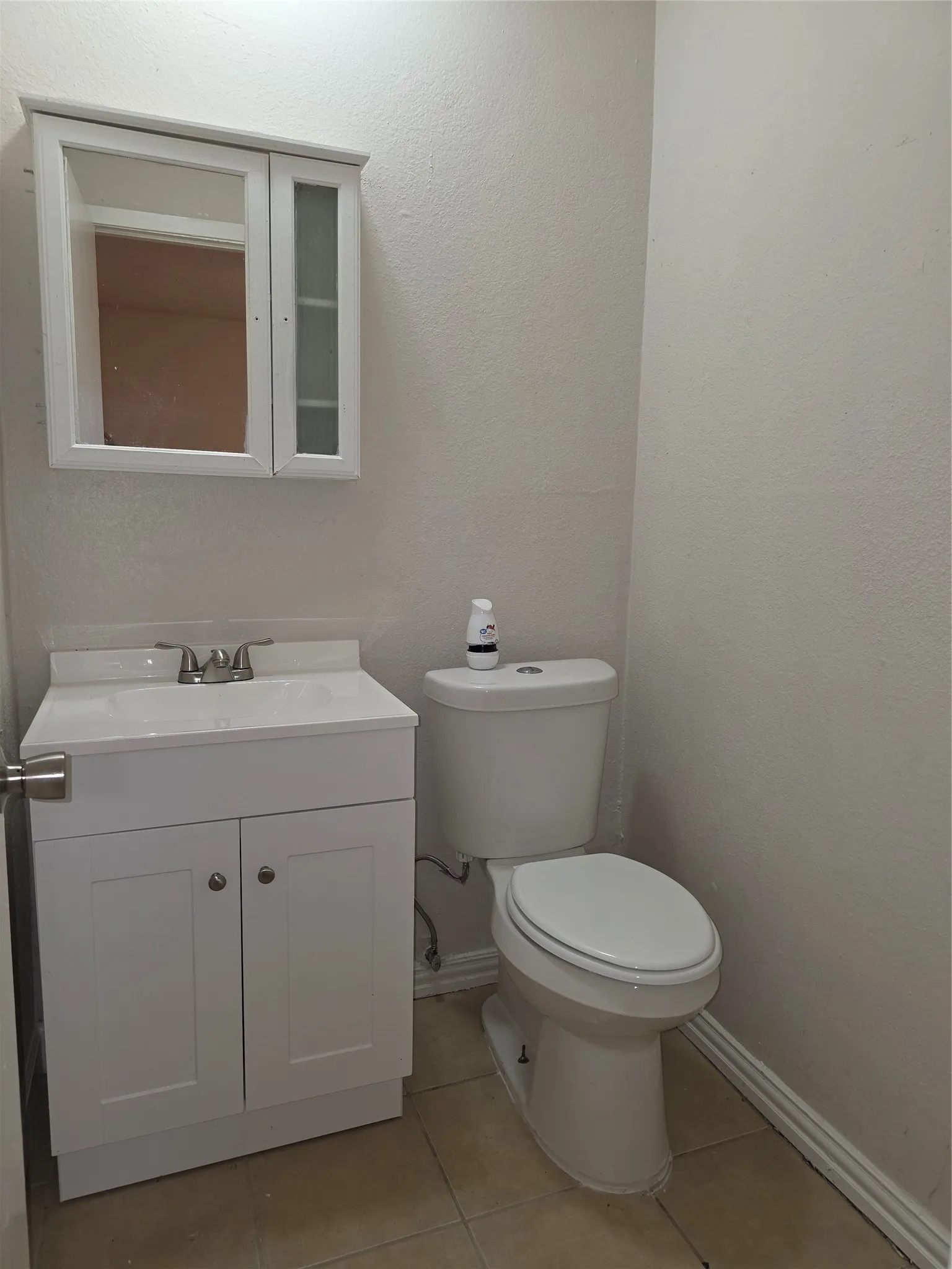 White vanity with integrated sink, coordinating wall-mounted medicine cabinet, white toilet, and neutral tile flooring