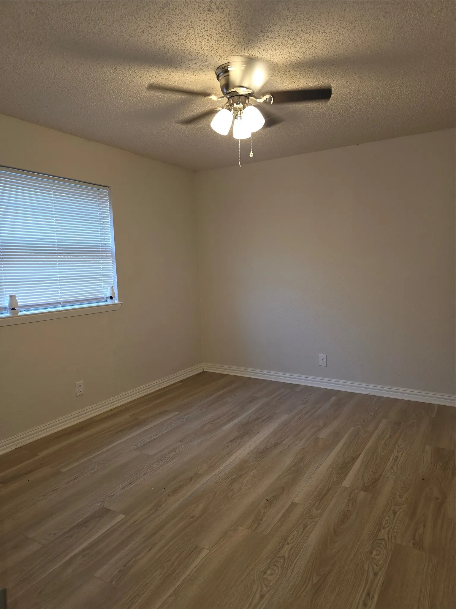 Wood-finish flooring, ceiling fan with integrated lighting, window with blinds, and neutral wall tones