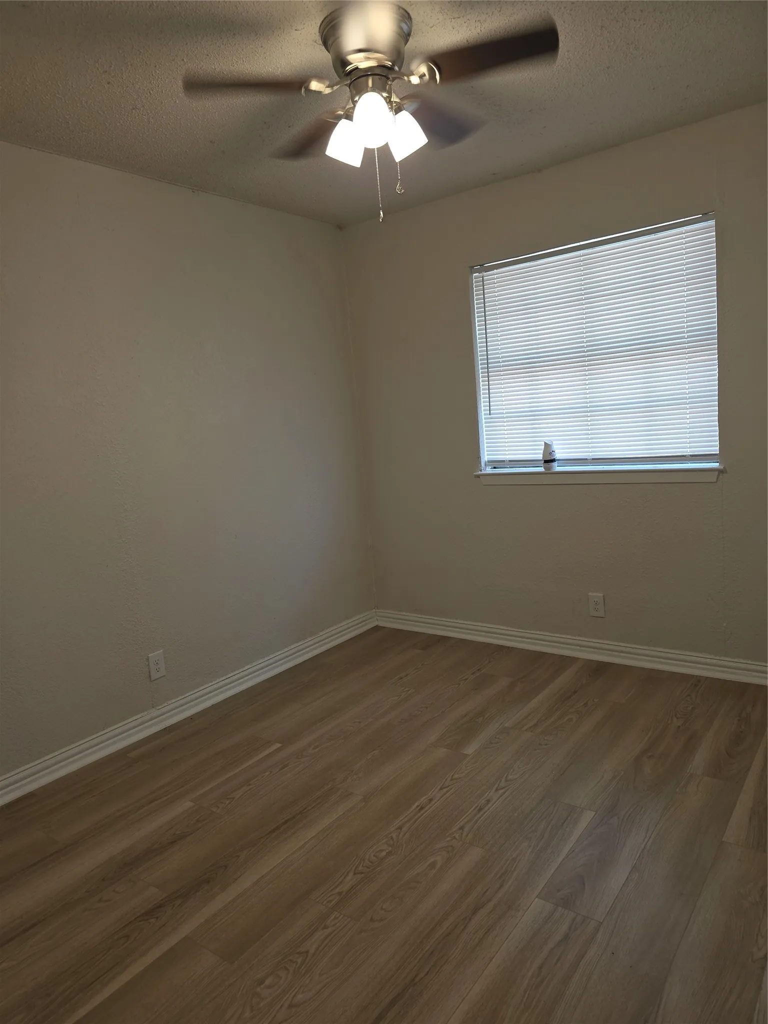 Wood-finish flooring, white trim, single window with blinds, and ceiling fan with integrated lighting