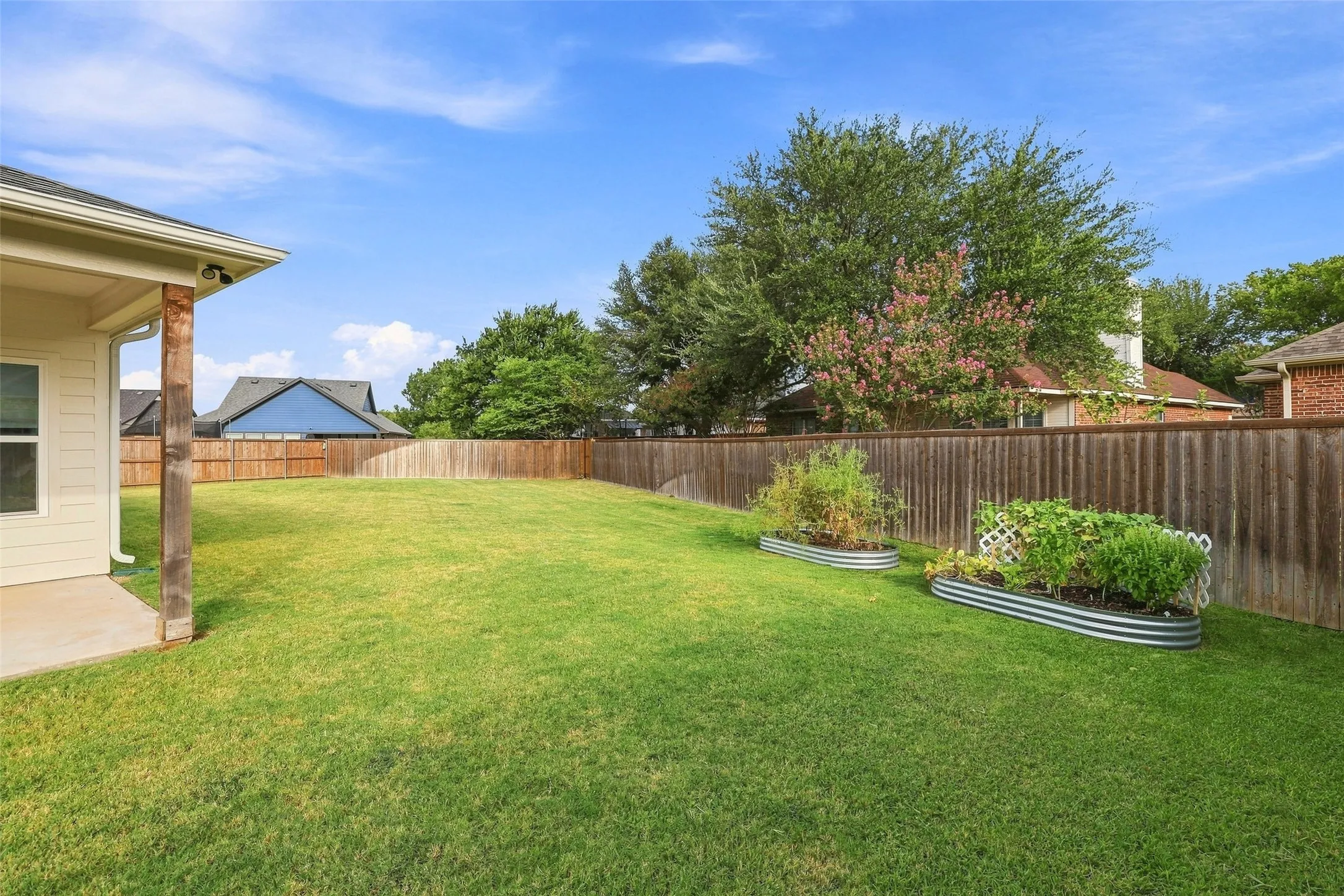 Expansive lawn area with raised garden beds, a privacy fence, and a concrete patio