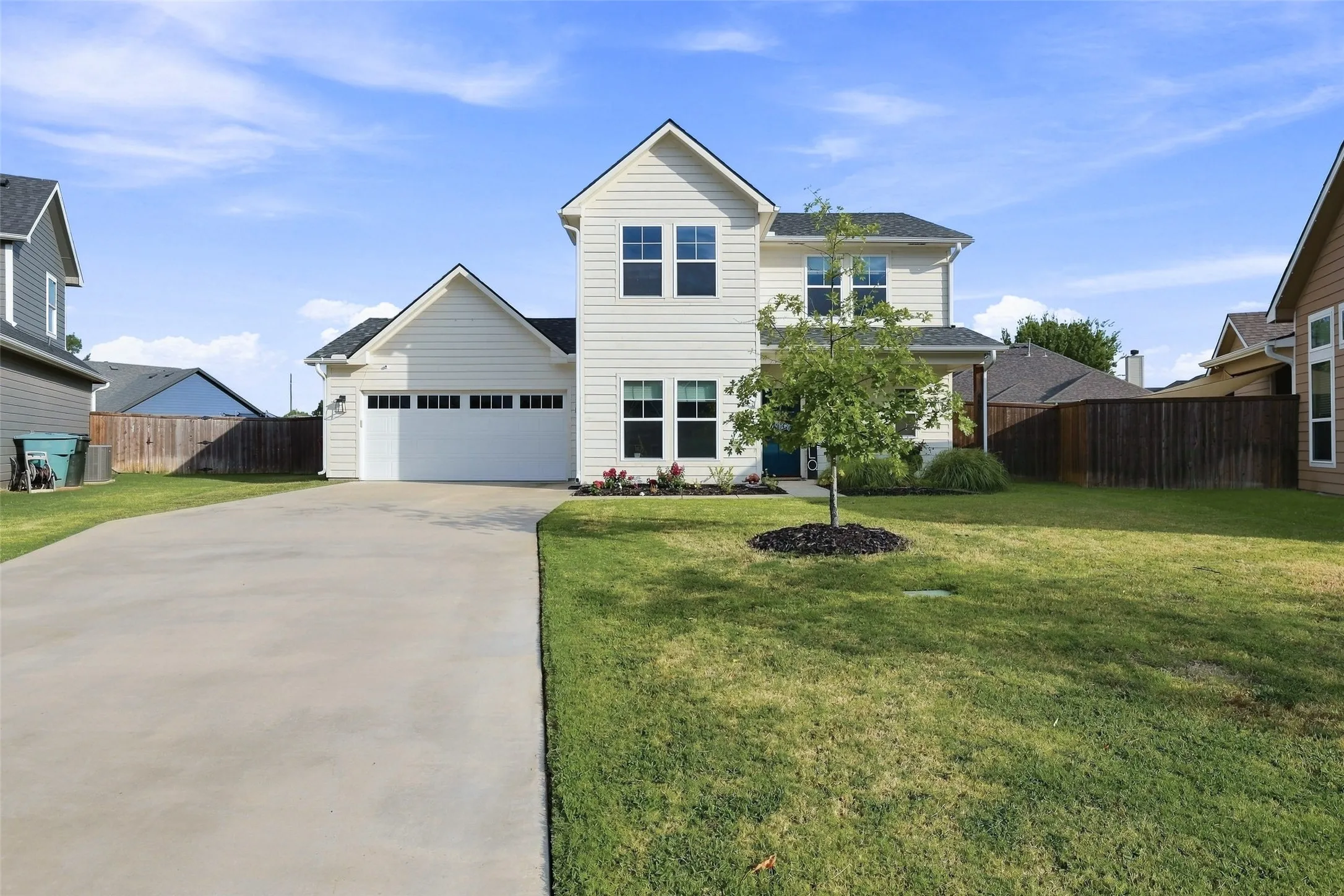 Two-story residence with a light-colored siding exterior, an attached two-car garage, a concrete driveway, a front lawn, and foundational landscaping