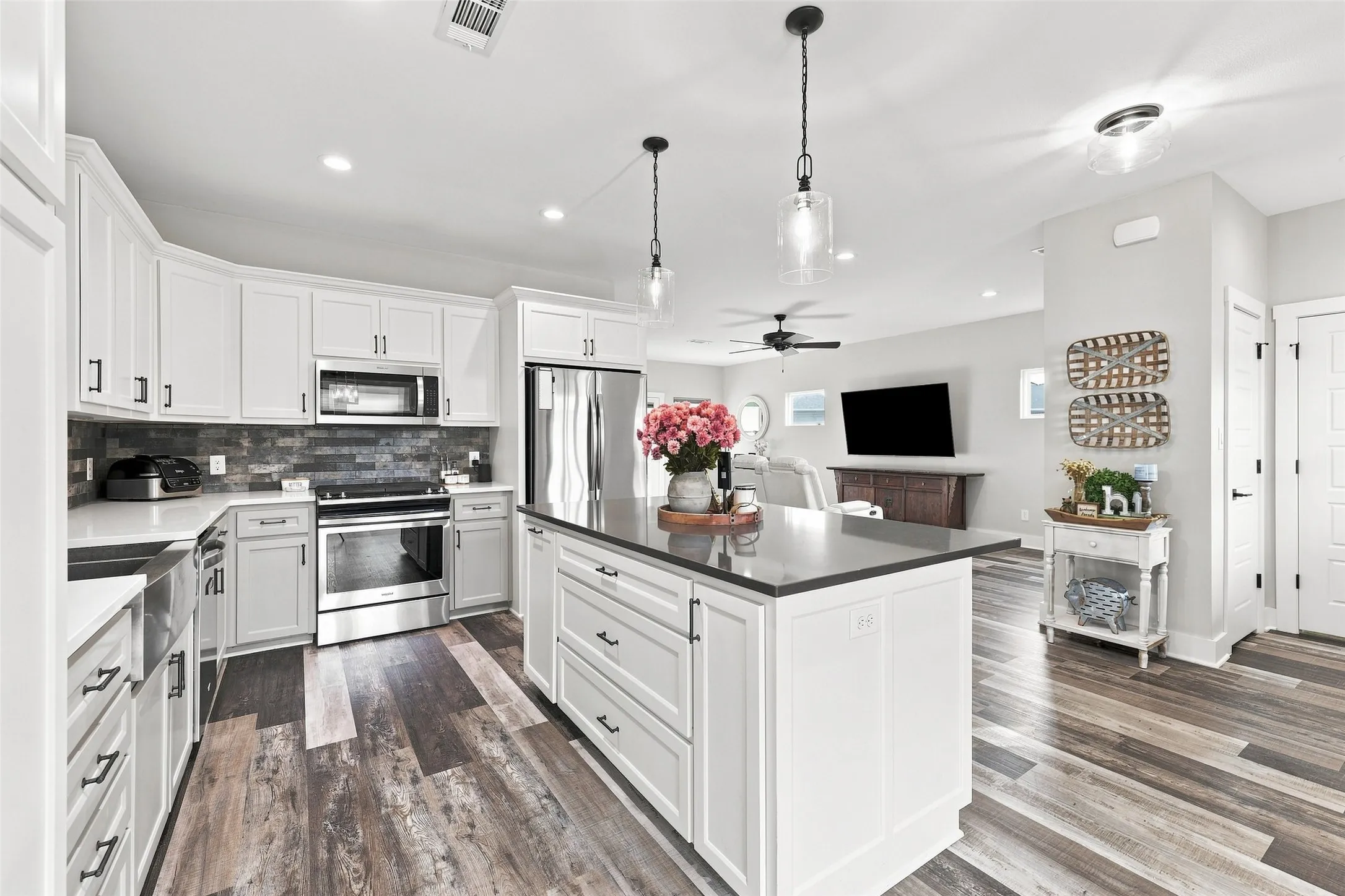 White shaker cabinetry, dark wood-finish flooring, stainless steel appliances, a center island with a dark countertop, and a tile backsplash