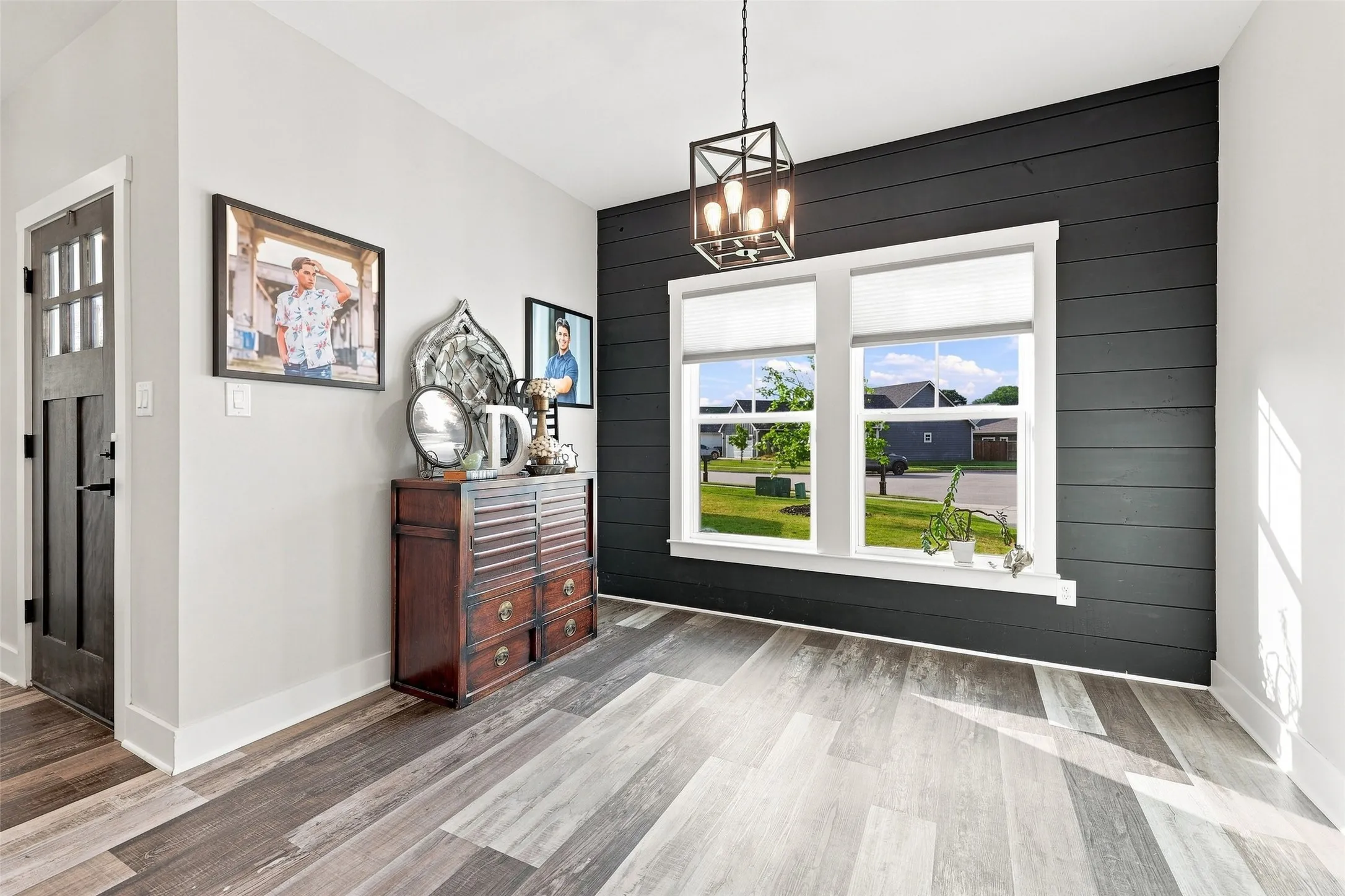 Accent wall with horizontal paneling, dual windows with white trim, wood-finish flooring, and a dark wood-paneled door