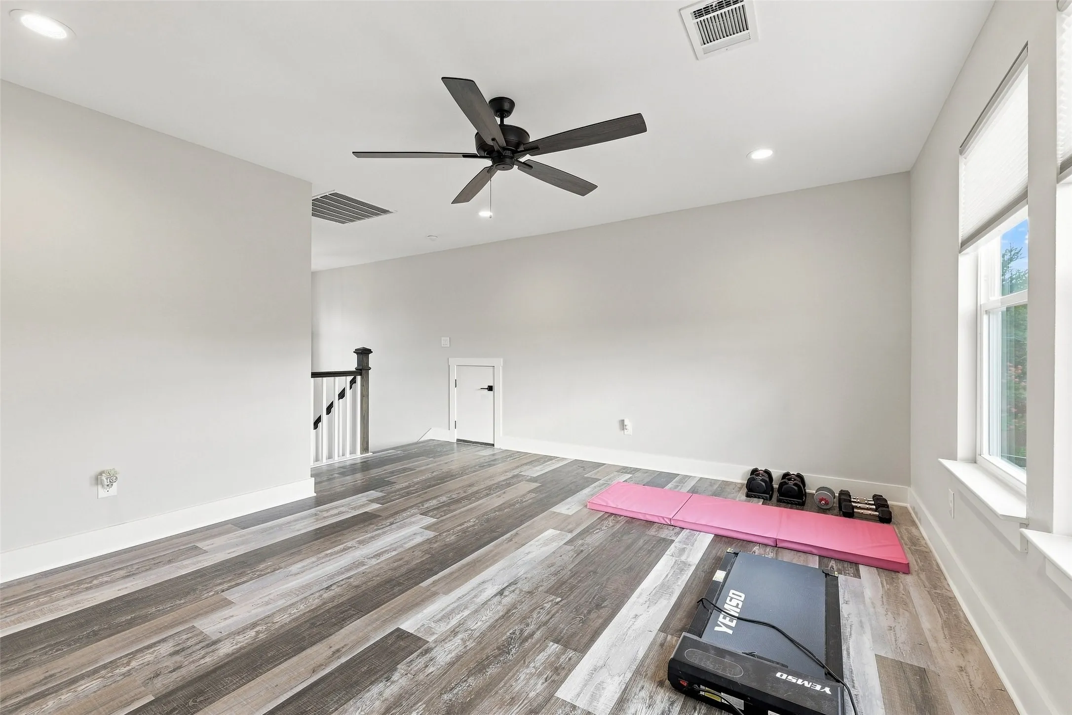 Spacious room with wood-finish flooring, recessed lighting, ceiling fan, and white trim