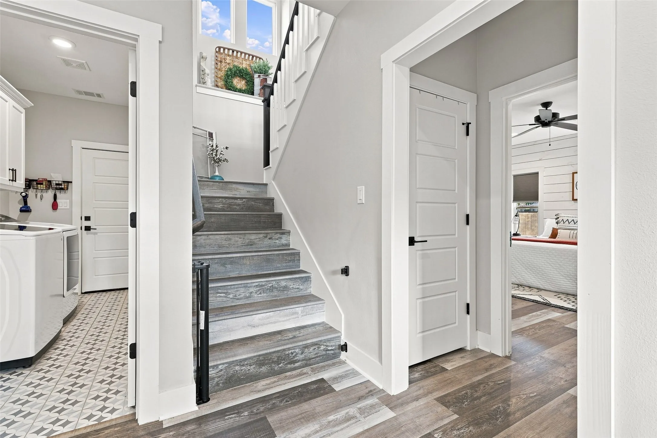 Wood-finish flooring with a light gray color palette, white trim, and a staircase featuring black metal spindles