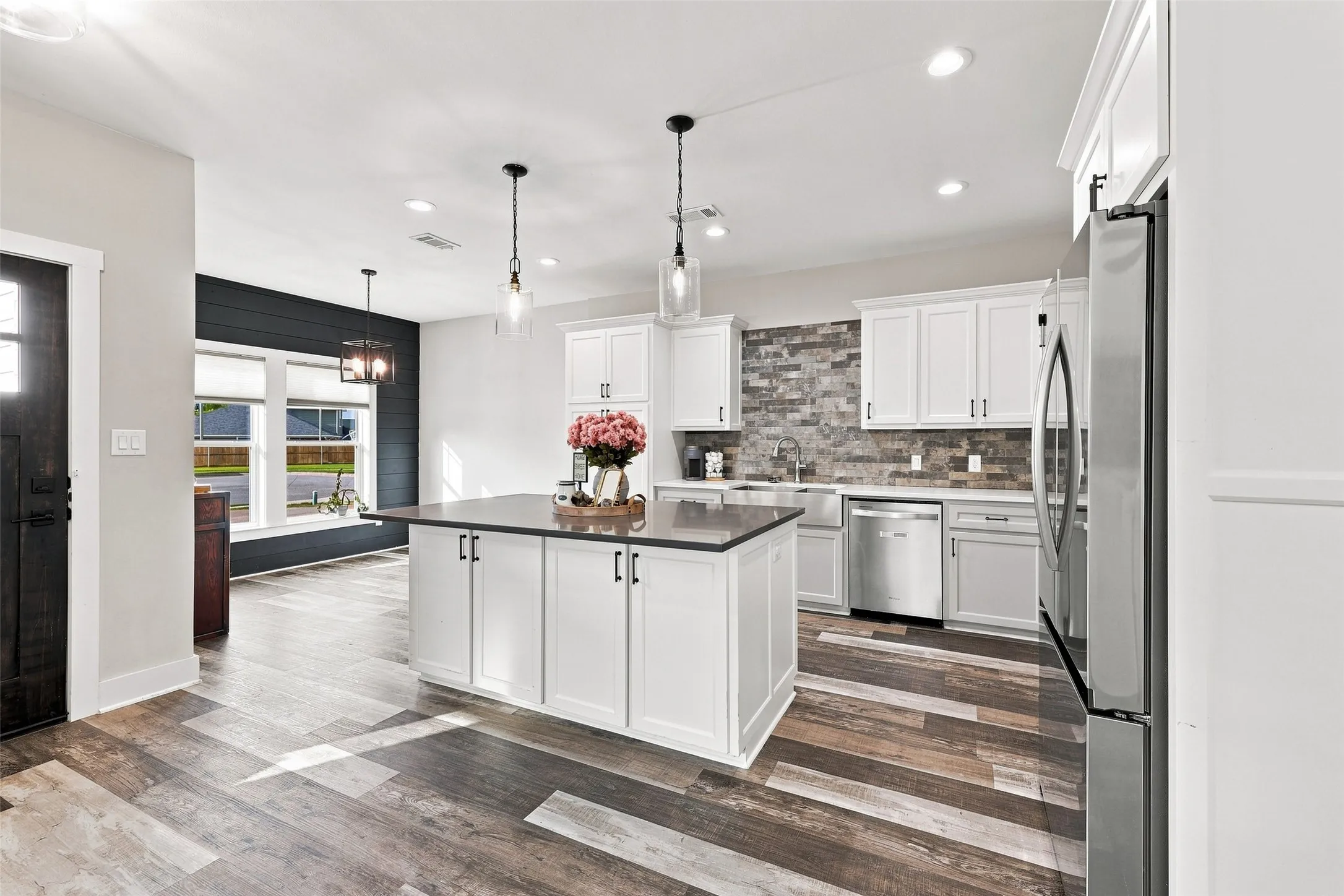 Kitchen featuring a central island with countertop, white cabinetry with dark hardware, stainless steel appliances, and wood-finish flooring