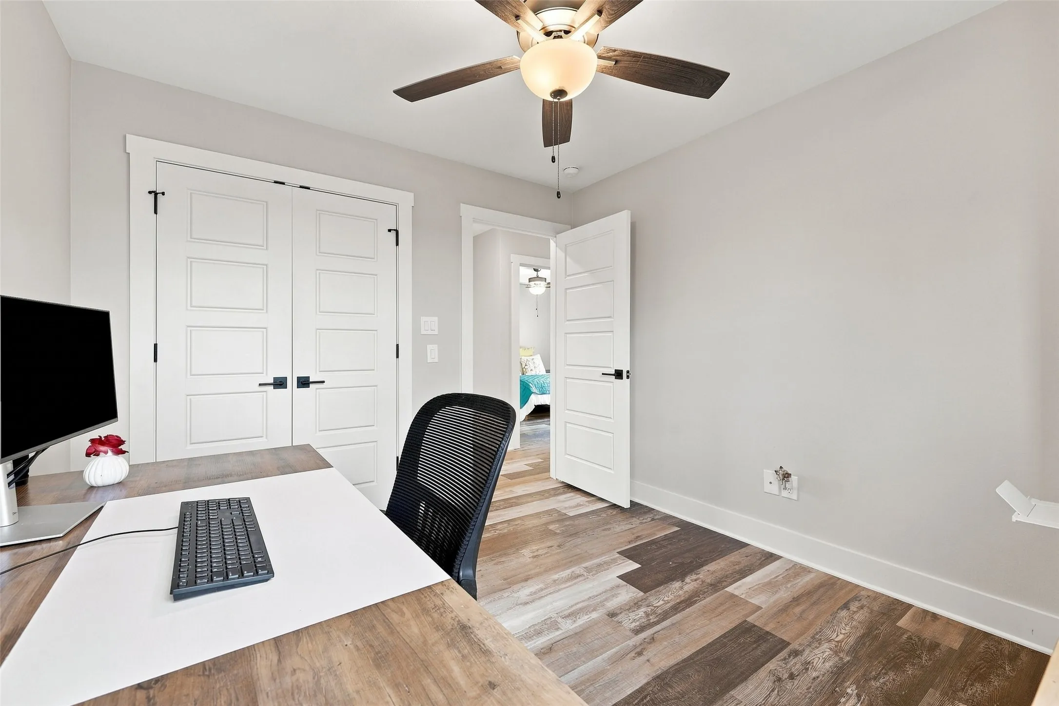Wood-finish flooring, ceiling fan with light fixture, white interior doors with black hardware, and light-colored wall paint
