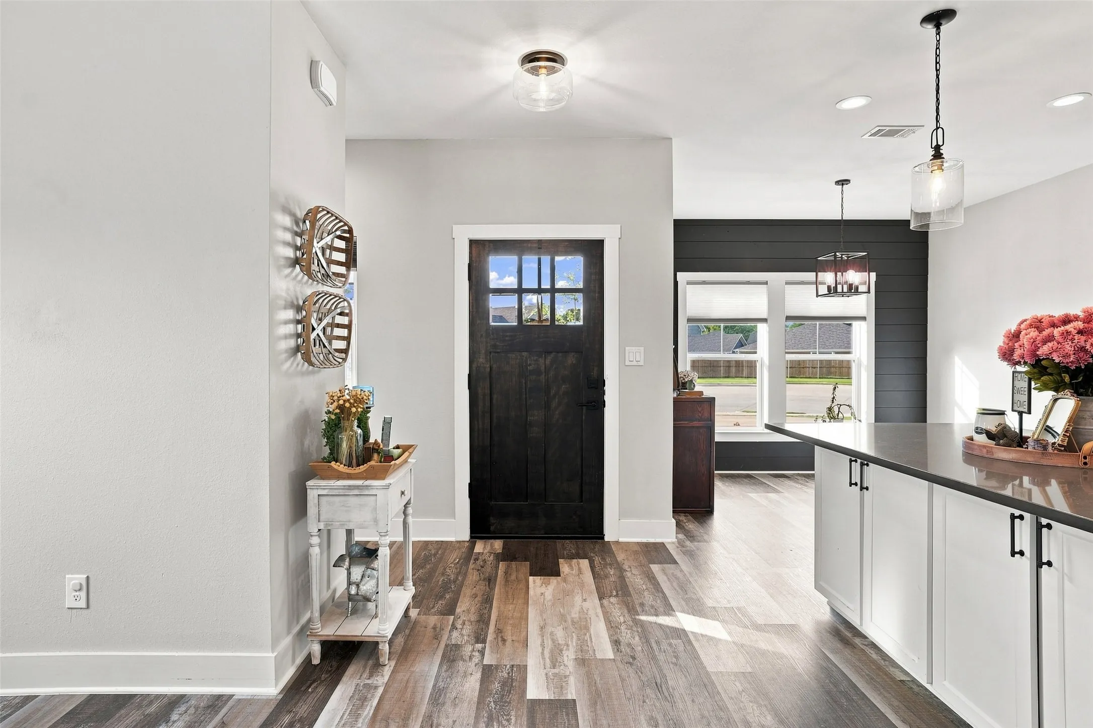 Wood-finish flooring, dark paneled entry door, white cabinetry with dark hardware, dark countertops, and pendant lighting