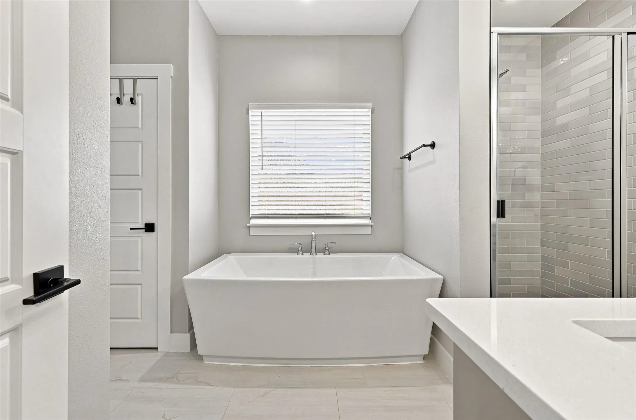 Freestanding soaking tub with polished chrome fixtures, separate shower with subway tile surround, and a vanity with a white countertop
