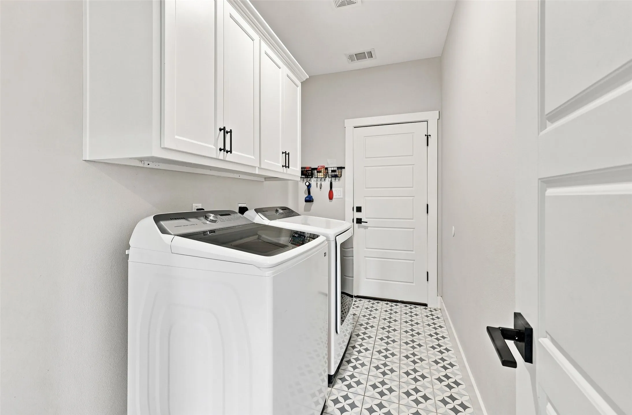 White shaker-style cabinetry with matte black hardware, geometric pattern floor tiling, white paneled door, and contemporary black door hardware