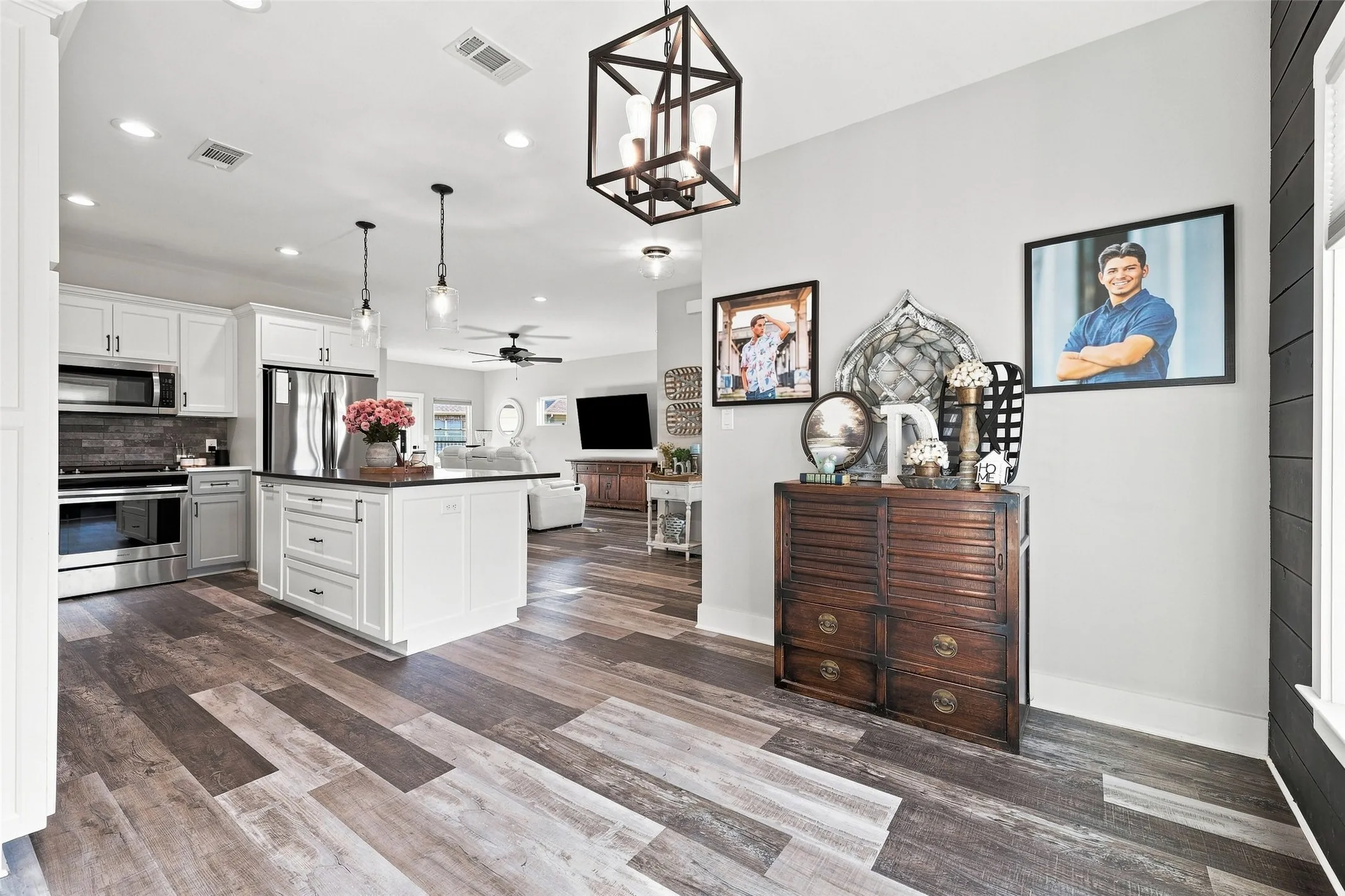 Spacious kitchen featuring white cabinetry, a large island with dark countertops, stainless steel appliances, and wood-finish flooring