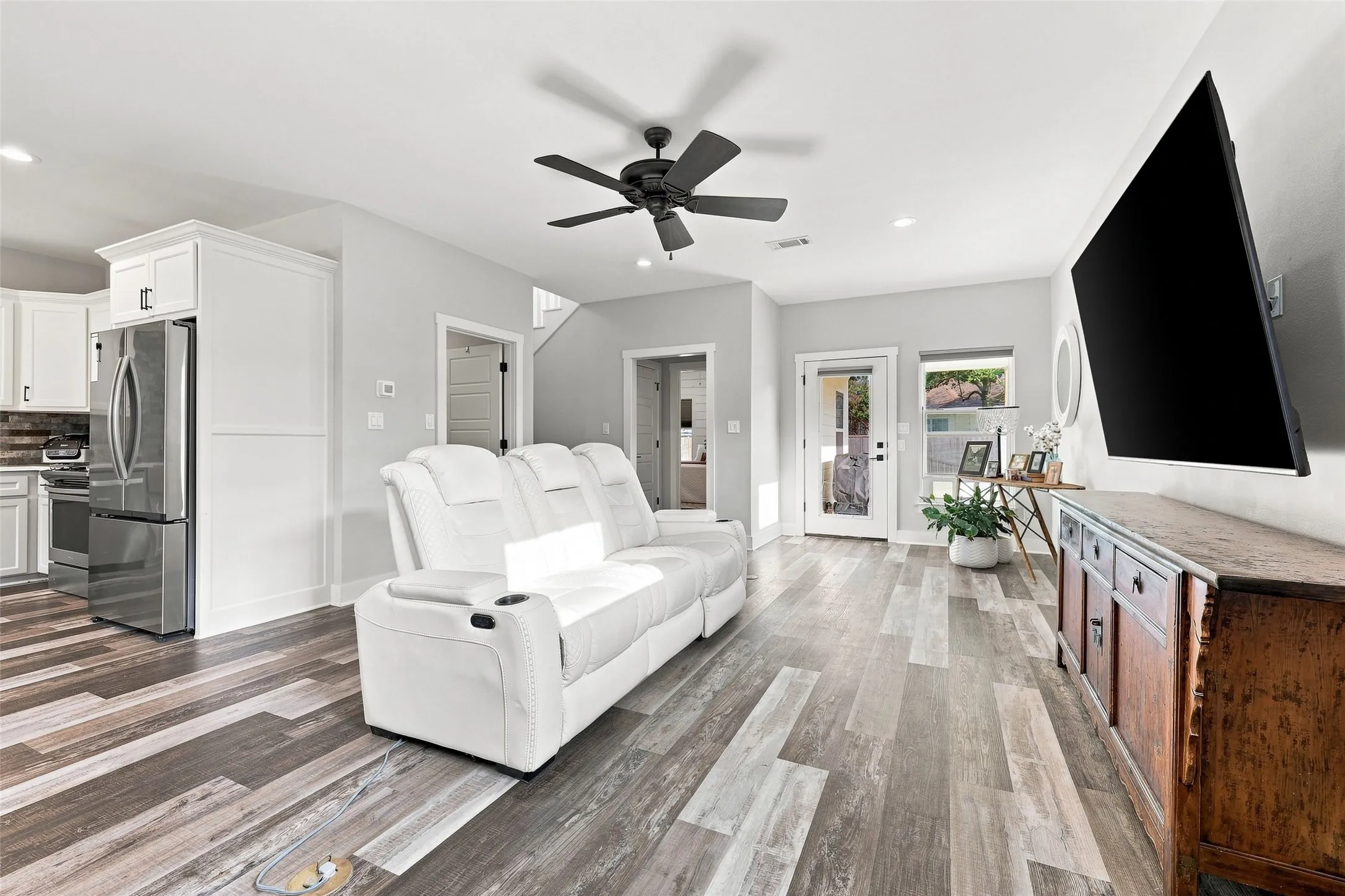 Open-concept living area featuring wood-finish flooring, a contemporary ceiling fan, recessed lighting, and a glass-paneled door