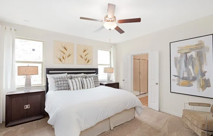 Bright bedroom featuring two large windows, a ceiling fan with integrated lighting, and carpet flooring