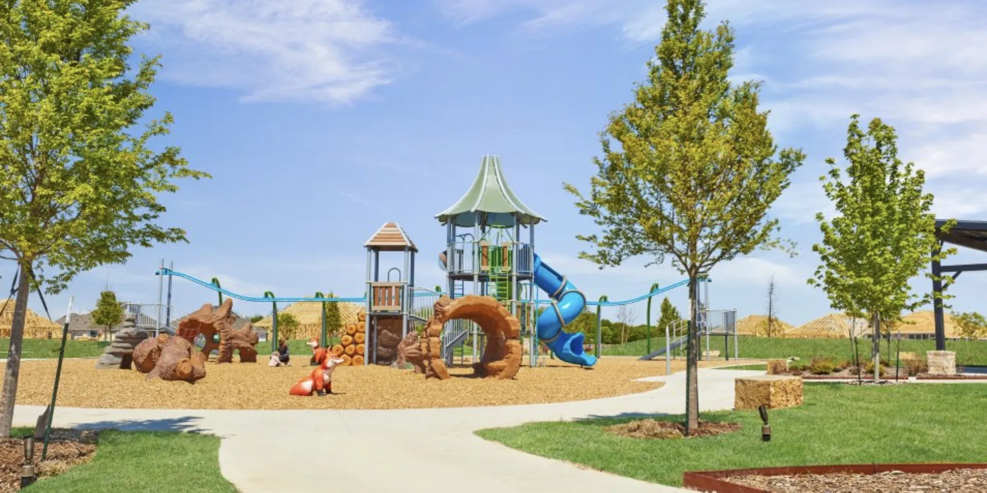 Community playground with multiple play structures, a winding paved pathway, and surrounding green spaces