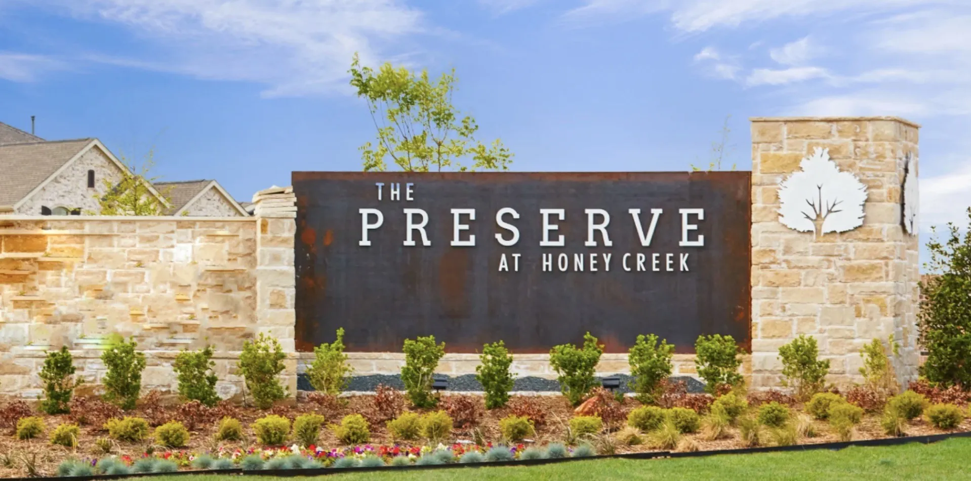 Stone facade entrance monument with an integrated metal sign, featuring a stylized tree emblem