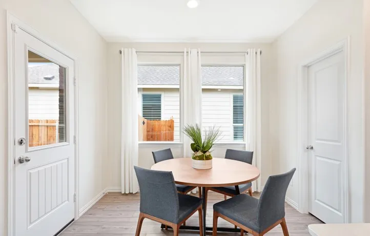 Bright dining area featuring wood-finish flooring, a white paneled door with glass insert, and two windows with white trim