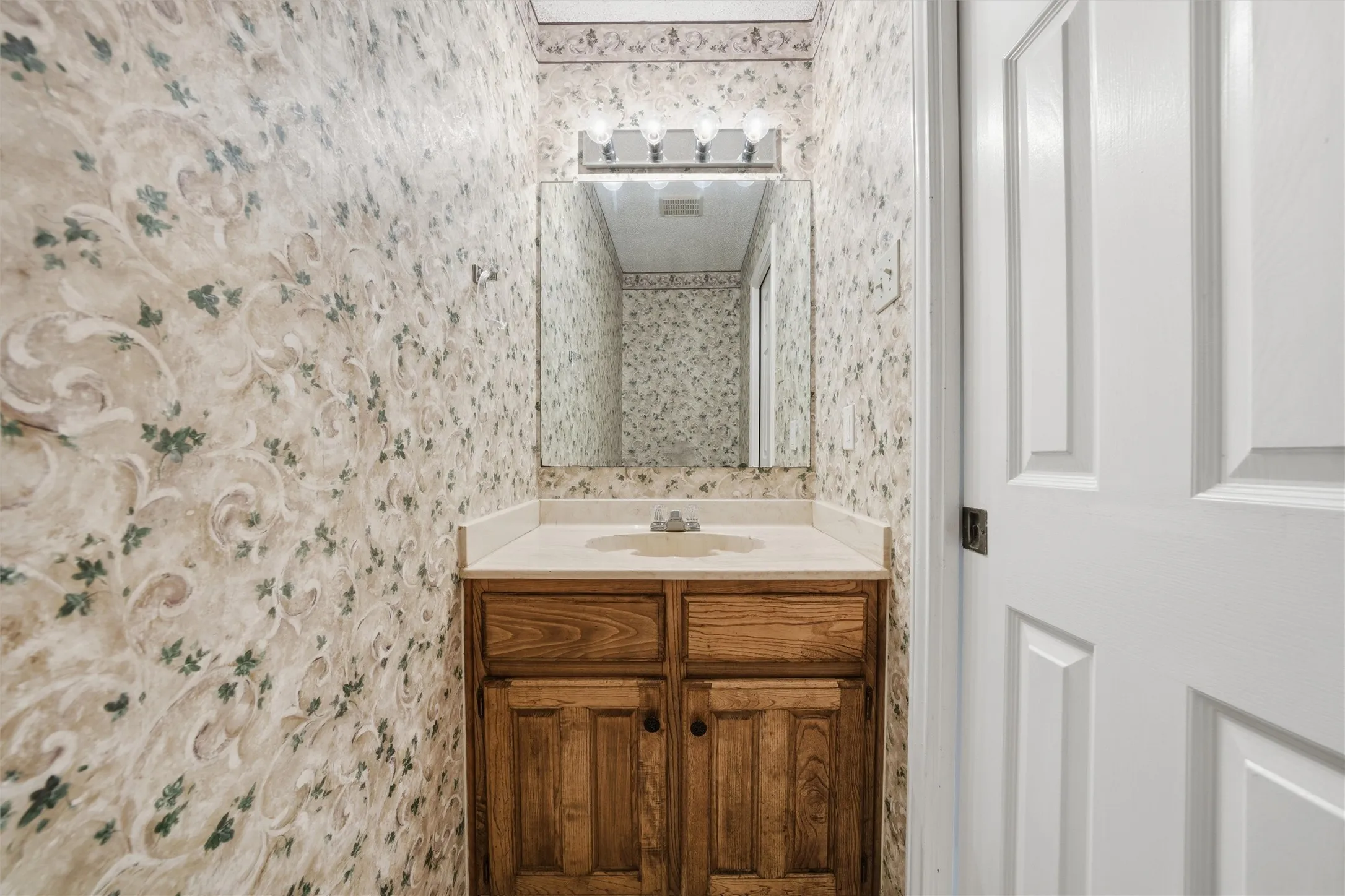 Wood-finish vanity with a built-in sink, framed mirror, and overhead lighting