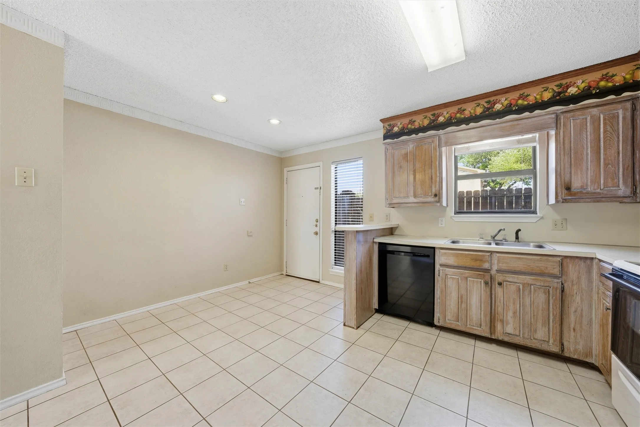 Kitchen featuring tile flooring, wood-finish cabinetry, a double basin sink, and a black dishwasher