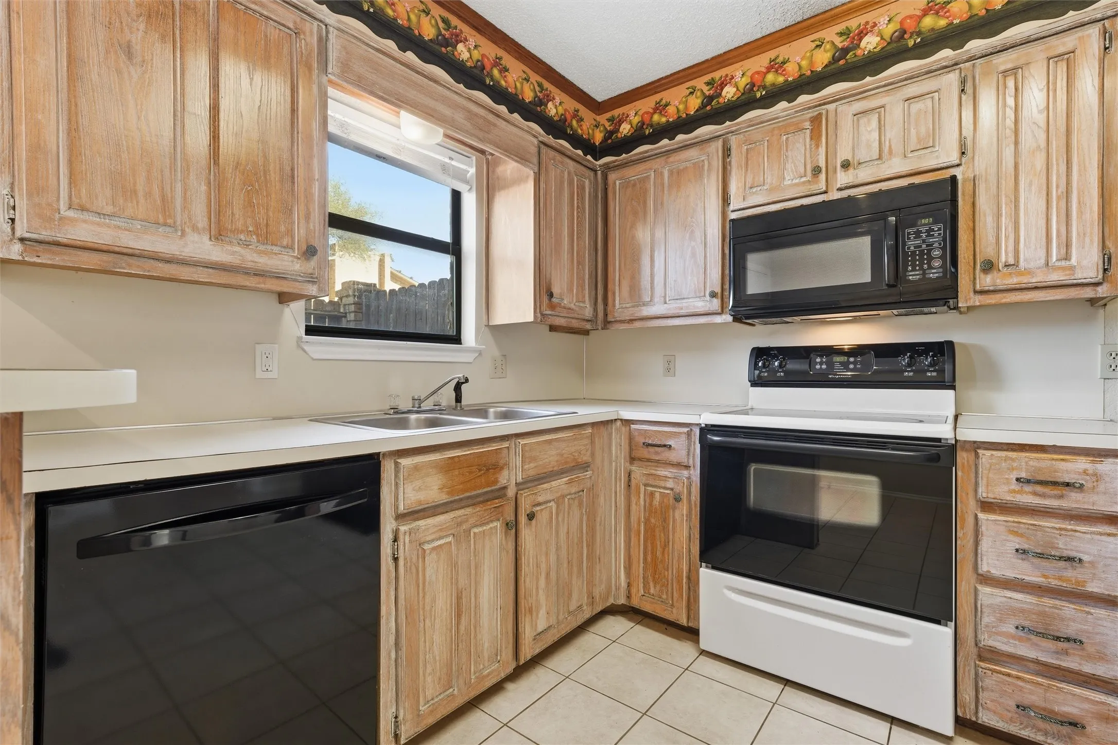 Kitchen featuring light wood-finish cabinetry, white countertops, a double basin sink, and tile flooring