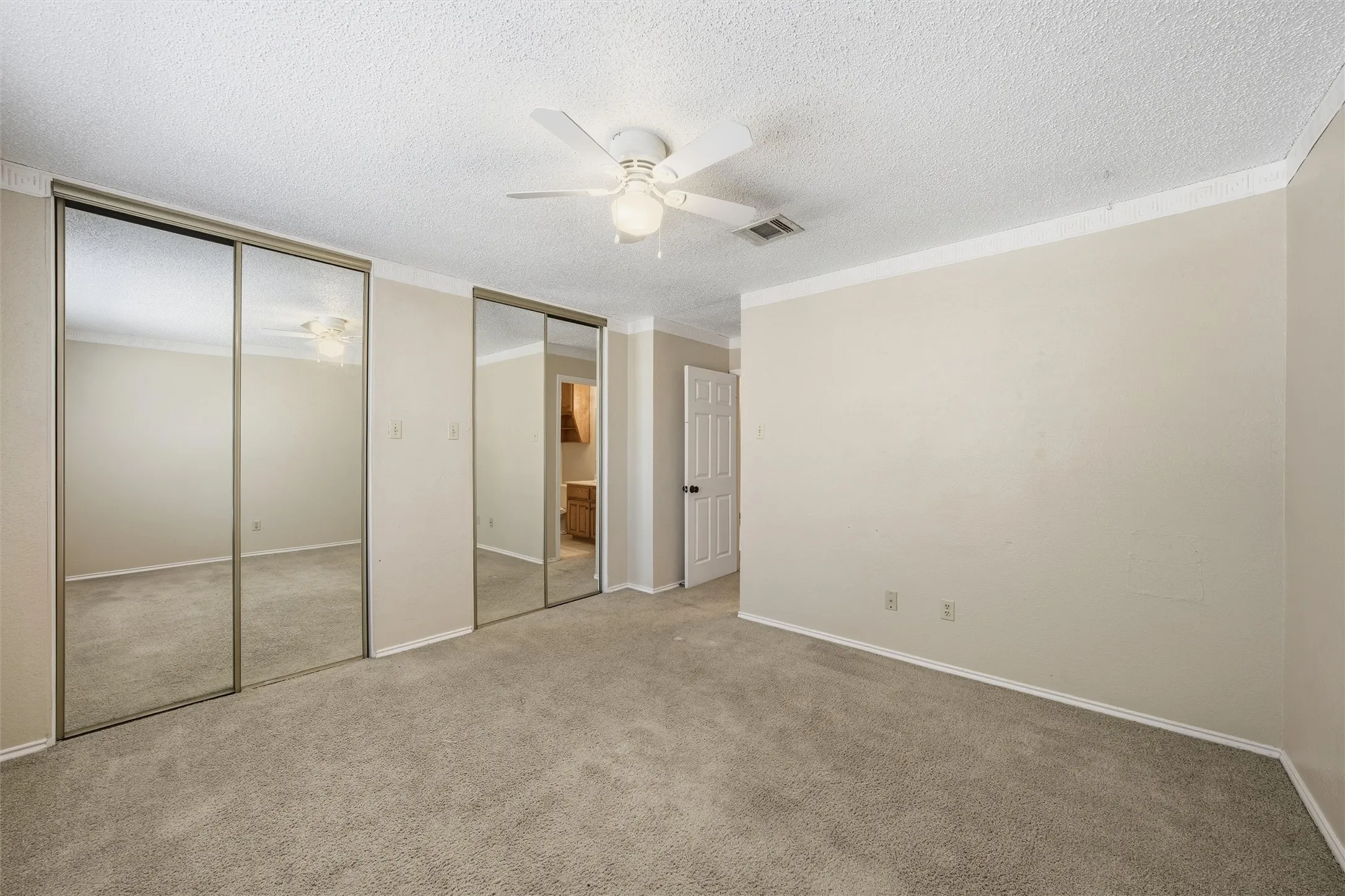 Spacious interior featuring neutral wall tones, carpet flooring, a ceiling fan, and mirrored closet doors