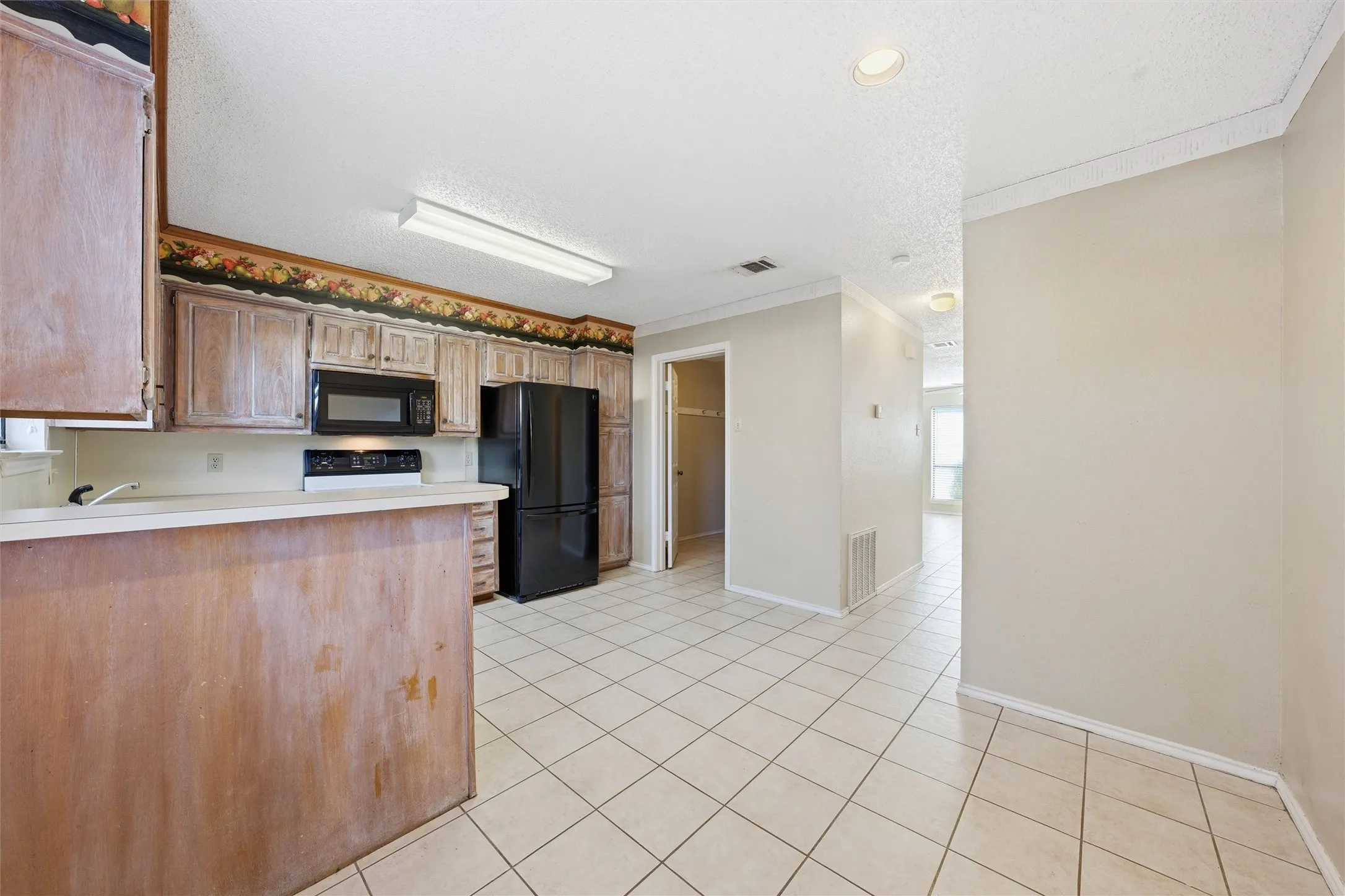 Kitchen featuring wood-finish cabinetry, black appliances, solid surface countertops, and white tile flooring